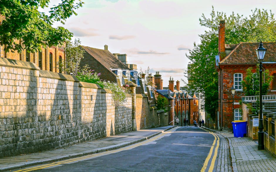 A narrow city street during daytime with tall buildings on either side, including a dark grey residential building on the left with small windows, and a modern red-brick office or apartment building o